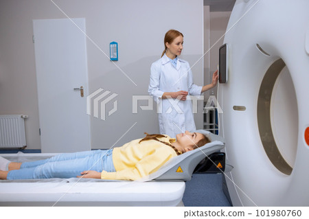 Little girl lying on table of mri scan machine female radiographer pushing button on control panel Little girl lying on table of mri scan machine female radiographer pushing button on control panel 101980760