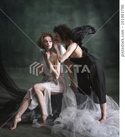 Devilish woman whispering to naive angel. Portrait of two women, angel and demon against dark, green, vintage background Devilish woman whispering to naive angel. Portrait of two women, angel and demon against dark, green, vintage background 101983786