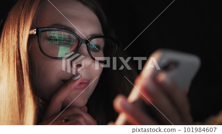 Beautiful young Woman Lying in Bed, Using Smart Phone and Smiling before Sleep. Woman using Cellphone on bed at Night. Attractive Girl looking at Mobile Phone 101984607