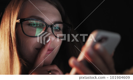 Beautiful young Woman Lying in Bed, Using Smart Phone and Smiling before Sleep. Woman using Cellphone on bed at Night. Attractive Girl looking at Mobile Phone 101984609