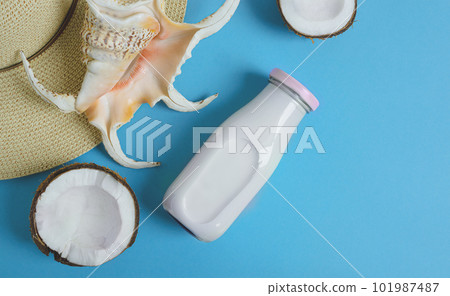 A bottle of vegan coconut milk, a piece of coconut, a summer hat and an exotic seashell on the blue background, top view with copy space A bottle of vegan coconut milk, a piece of coconut, a summer hat and an exotic seashell on the blue background, top view with copy space 101987487