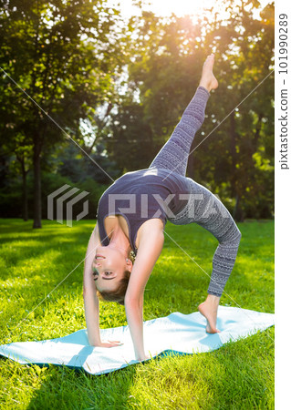Young woman doing yoga exercises in the summer city park. 101990289