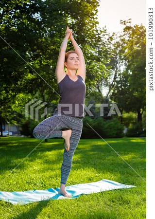 Young woman doing yoga exercises in the summer city park. 101990313