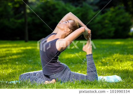 Young woman doing yoga exercises in the summer city park. 101990334