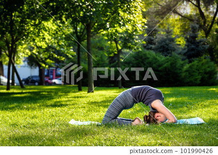Young woman doing yoga exercises in the summer city park. 101990426