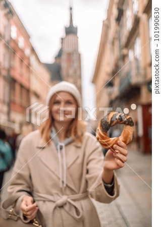 Happy young blonde woman tourist in stylish clothes holding pretzel obwarzanek on the market square in Krakow in Poland Happy young blonde woman tourist in stylish clothes holding pretzel obwarzanek on the market square in Krakow in Poland 101990630
