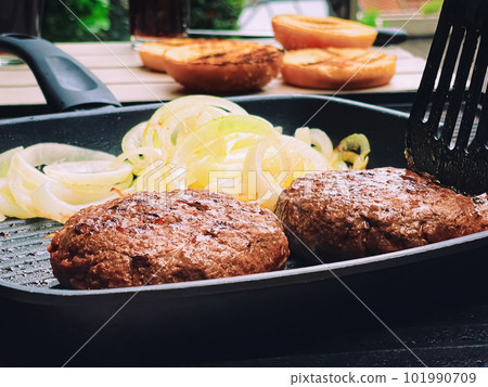 Cooking minced beef burger on cast iron grill skillet outdoors, red meat on frying pan, grilling food in the garden, English countryside living 101990709