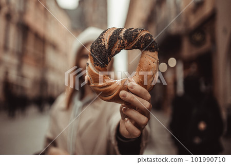 Happy young blonde woman tourist in stylish clothes holding pretzel obwarzanek on the market square in Krakow in Poland 101990710