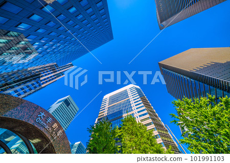 日本的東京城市景觀 陽光如夏。大手町十字路口前的大手町站和在藍天和新綠中閃耀的摩天大樓=四月 101991103