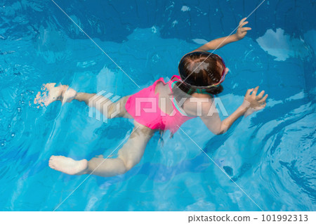 Young girl floating in blue pool water in motion among splashes of water 101992313