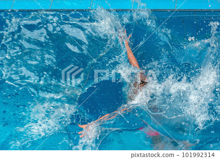 Young girl floating in blue pool water in motion among splashes of water 101992314