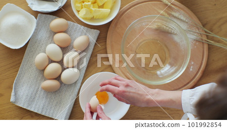 Woman cracking an egg into flour to make bread according to traditional recipe. Woman baking at home, enjoying hobby. Woman cracking an egg into flour to make bread according to traditional recipe. Woman baking at home, enjoying hobby. 101992854