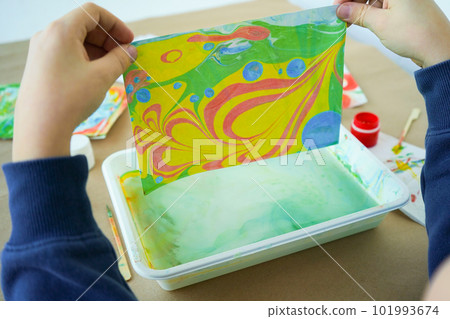 Boy is drawing Ebru and set of tools on table. Traditional Turkish Ebru technique. top view. Children development concept Boy is drawing Ebru and set of tools on table. Traditional Turkish Ebru technique. top view. Children development concept 101993674