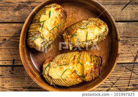Hasselback potatoes with cheese, garlic and herbs. Wooden background. Top view Hasselback potatoes with cheese, garlic and herbs. Wooden background. Top view 101997825