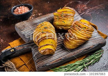 Roasted Hasselback Potato with Fresh thyme and rosemary. Dark background. Top view 101997863
