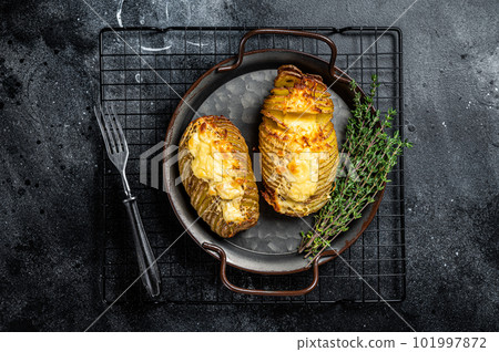 Baked hasselback potatoes with cheese, garlic, thyme and rosemary. Black background. Top view 101997872