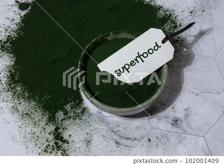 Blue-green algae Chlorella and spirulina powder in bowl with paper note text SUPERFOOD. Super powder. Natural supplement of algae. Detox superfood drink cocktail. Food supplement source of protein and Blue-green algae Chlorella and spirulina powder in bowl with paper note text SUPERFOOD. Super powder. Natural supplement of algae. Detox superfood drink cocktail. Food supplement source of protein and 102001409