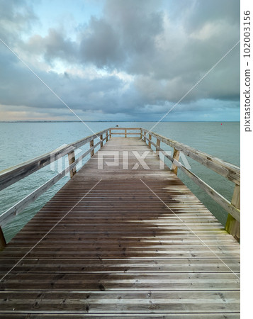 Empty wooden pier with dramatic sky and calm water Empty wooden pier with dramatic sky and calm water 102003156