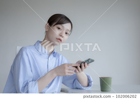 Portrait of a young woman sitting with a smartphone Portrait of a young woman sitting with a smartphone 102006202