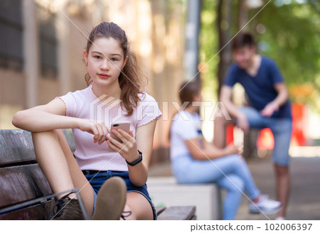Portrait of teenage girl using smartphone on the bench at sunny day 102006397