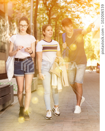 Happy teenagers strolling through city streets on summer day 102006539