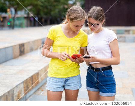 Teenager girls using smartphones while standing in park Teenager girls using smartphones while standing in park 102006934