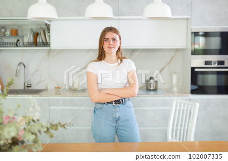 Portrait of long-haired young woman inwhite T-shirt, standing in kitchen 102007335