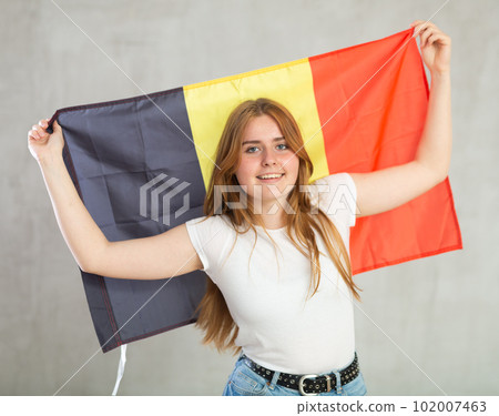 smiling girl in arms raised above head holds canvas of national flag of Belgium. 102007463