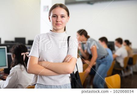 Confident interested female student standing in technology classroom against background of rows of computers on desks 102008034