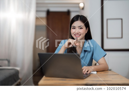 Beautiful Asian woman relaxing using laptop computer while sitting on table creative woman working and typing on keyboard at home working at home concept Beautiful Asian woman relaxing using laptop computer while sitting on table creative woman working and typing on keyboard at home working at home concept 102010574