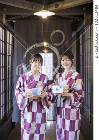 A young woman in a yukata standing in front of a noren with a bath tub and a towel 102011484