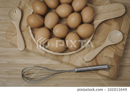 Kitchen metal wire and raw eggs on the wooden board 102011649