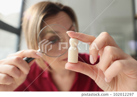 Focused woman examines small wooden figure with magnifier Focused woman examines small wooden figure with magnifier 102012297
