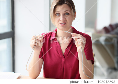 Upset woman holds broken cable sitting at table in office 102012298