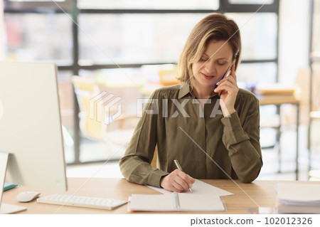 Woman listens to client on phone making notes with pen Woman listens to client on phone making notes with pen 102012326