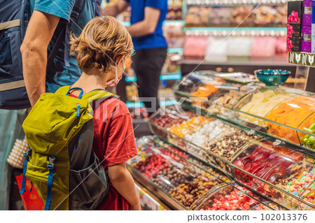 The boy looks at the counter with Turkish sweets. Traditional oriental sweet pastry cookies, nuts, dried fruits, pastilles, marmalade, Turkish desert with sugar, honey and pistachio, in display at a 102013376