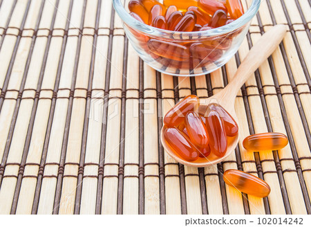 Fish oil capsules in wooden spoon on bamboo mat 102014242