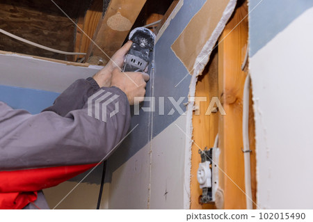 Worker cutting drywall plasterboard with using multi tool 102015490