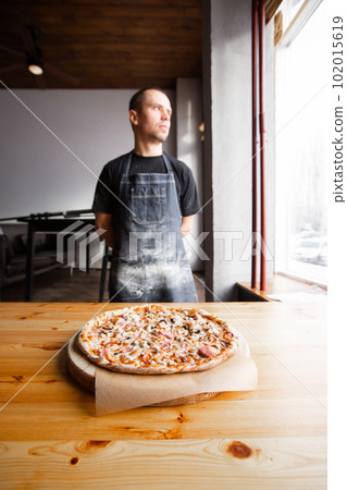 chef baker in uniform blue apron cutting pizza at kitchen 102015619
