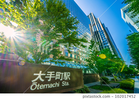 日本的東京城市景觀 陽光如夏。 “大手町”十字路口前的大手町站和在新綠中閃耀的摩天大樓=四月 102017452