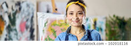 Pleased young woman, female artist in apron smiling at camera, posing with her hands in paint, standing at home studio workshop 102018116