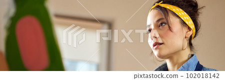 Portrait of creative young woman in apron looking at her work while working on abstract painting at cozy workshop Portrait of creative young woman in apron looking at her work while working on abstract painting at cozy workshop 102018142