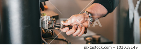 Barista grinds coffee beans pouring into a portafilter using coffee machine 102018149