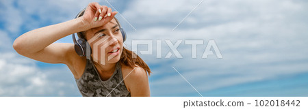 Tired female runner in headphones sweating after cardio exercise and rest after finish on beach Tired female runner in headphones sweating after cardio exercise and rest after finish on beach 102018442