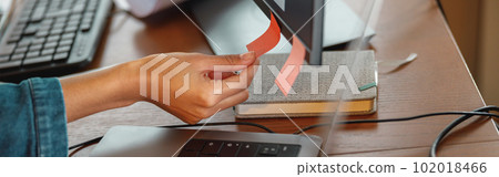 Close up of woman hand glues sticky stickers on computer while sitting at home office table Close up of woman hand glues sticky stickers on computer while sitting at home office table 102018466