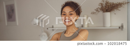 Slim woman doing exercises for hands with elastic band by online tutorials on laptop in living room 102018475