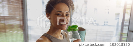 Woman drink water and holding rolled fitness mat after working out at home 102018520