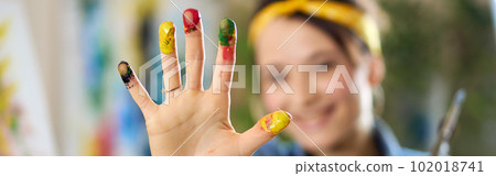 Cheerful woman smiling, creating abstract painting, applying colorful paints on canvas with fingers. Selective focus on hand in paint 102018741
