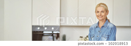 Smiling woman in rubber gloves ready for clean up in the kitchen. Detergents, sanitizer spray and gel in bottle on the surface 102018913
