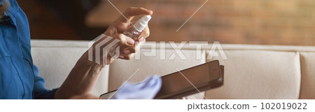 Close up shot of hands of woman disinfecting and cleaning tablet pc from microbes, viruses and bacteria with a disinfectant 102019022